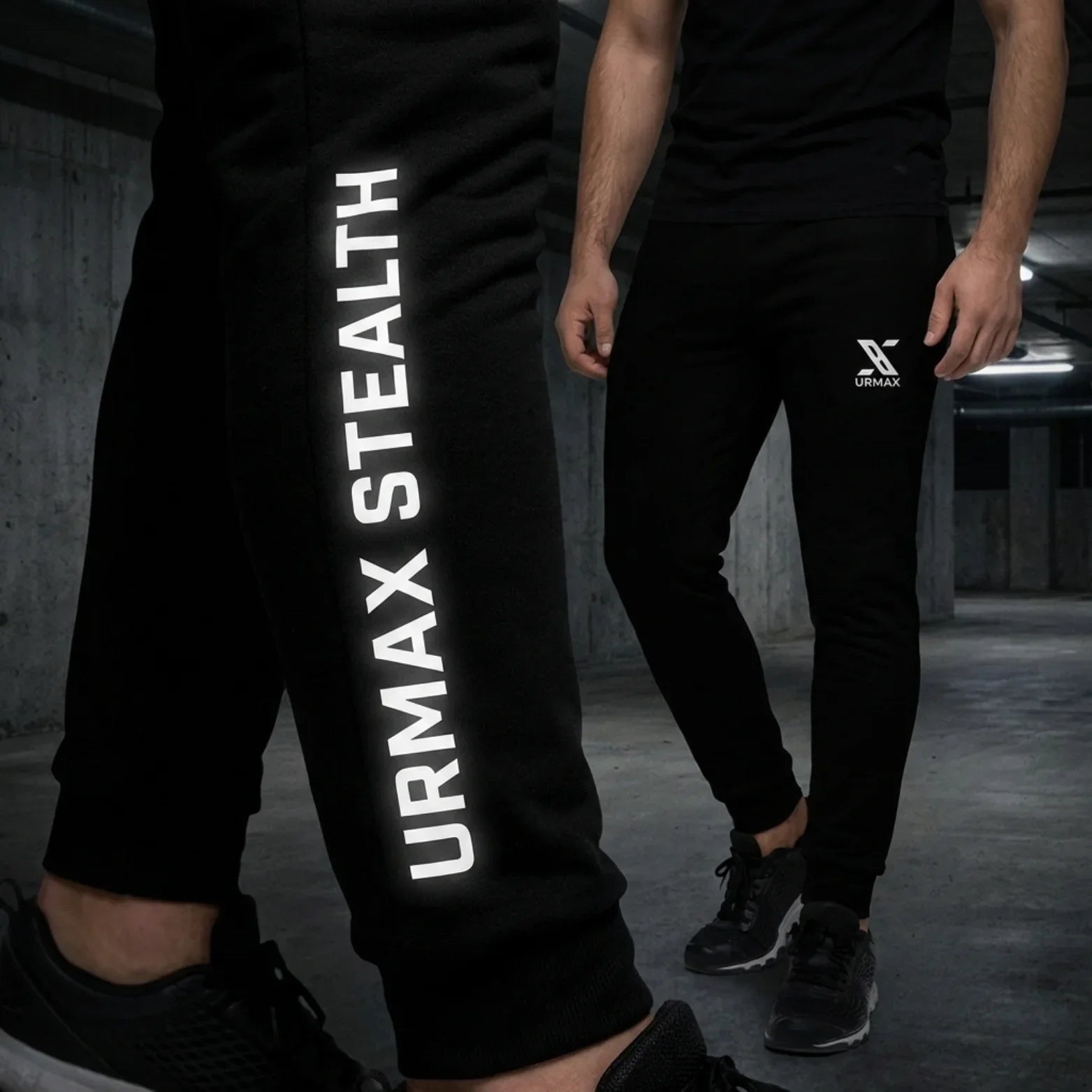 Man wearing black URMAX Stealth joggers with bold white logo in an industrial setting