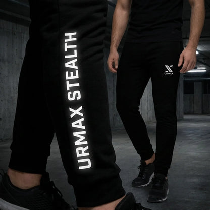 Man wearing black URMAX Stealth joggers with bold white logo in an industrial setting