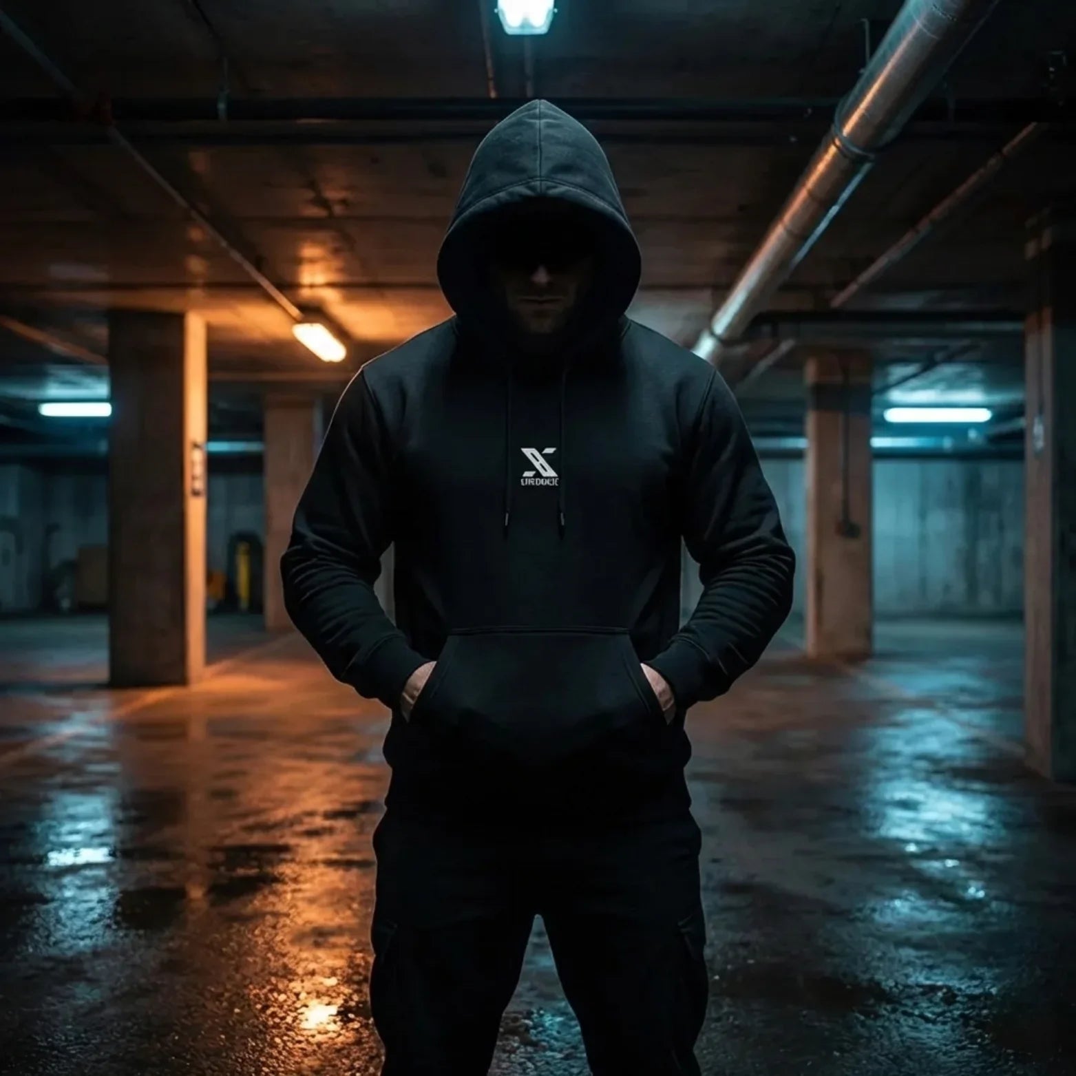 Man in black URMAX TACTIKAL hoodie standing in a dimly lit parking garage