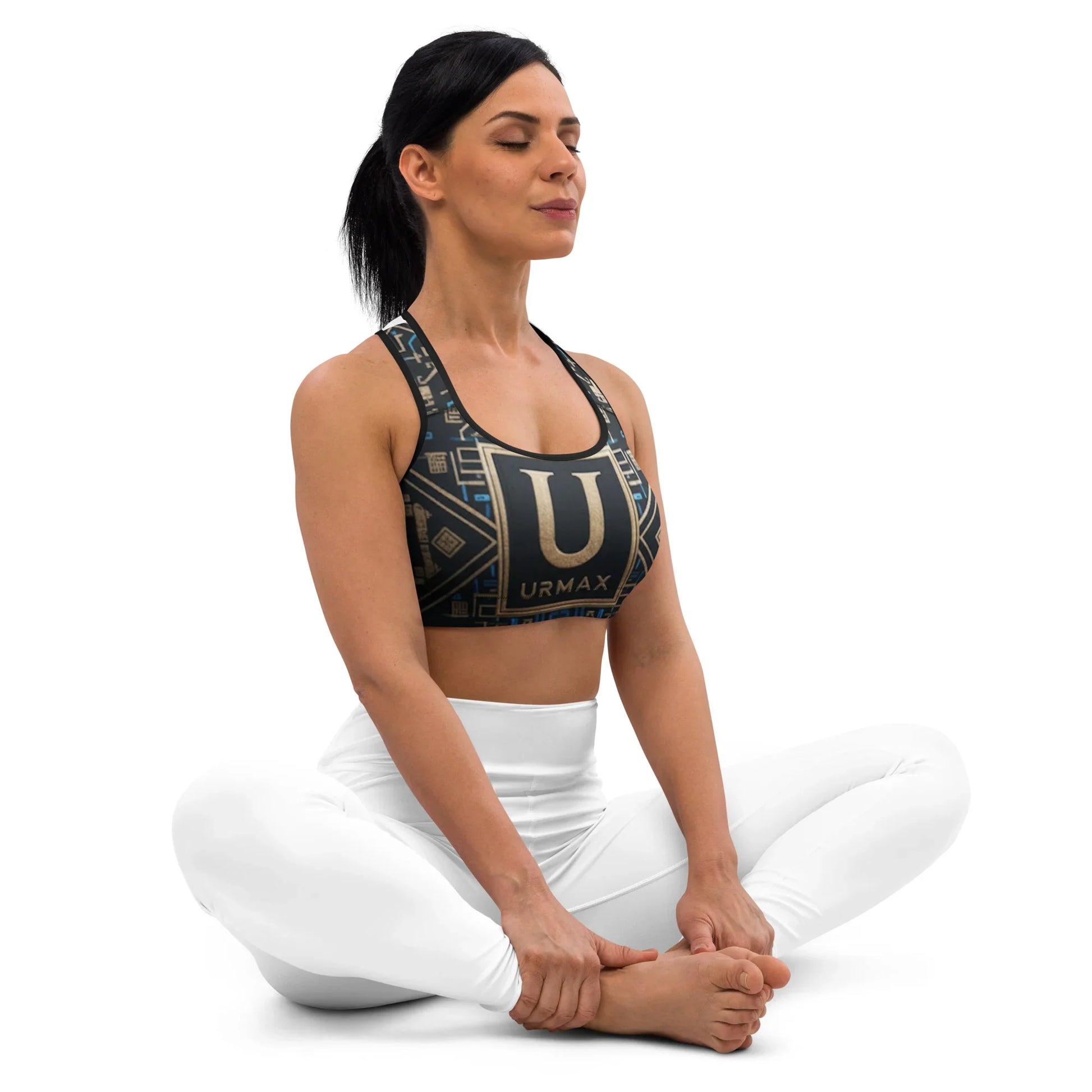 Woman in black URMAX sports bra and white leggings sitting cross-legged in yoga pose