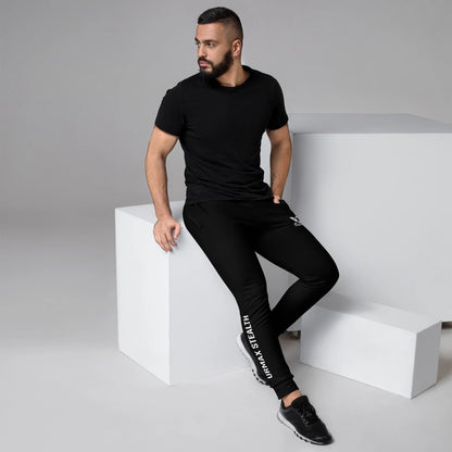 Man wearing black URMAX STEALTH joggers and black t-shirt sitting on white cube