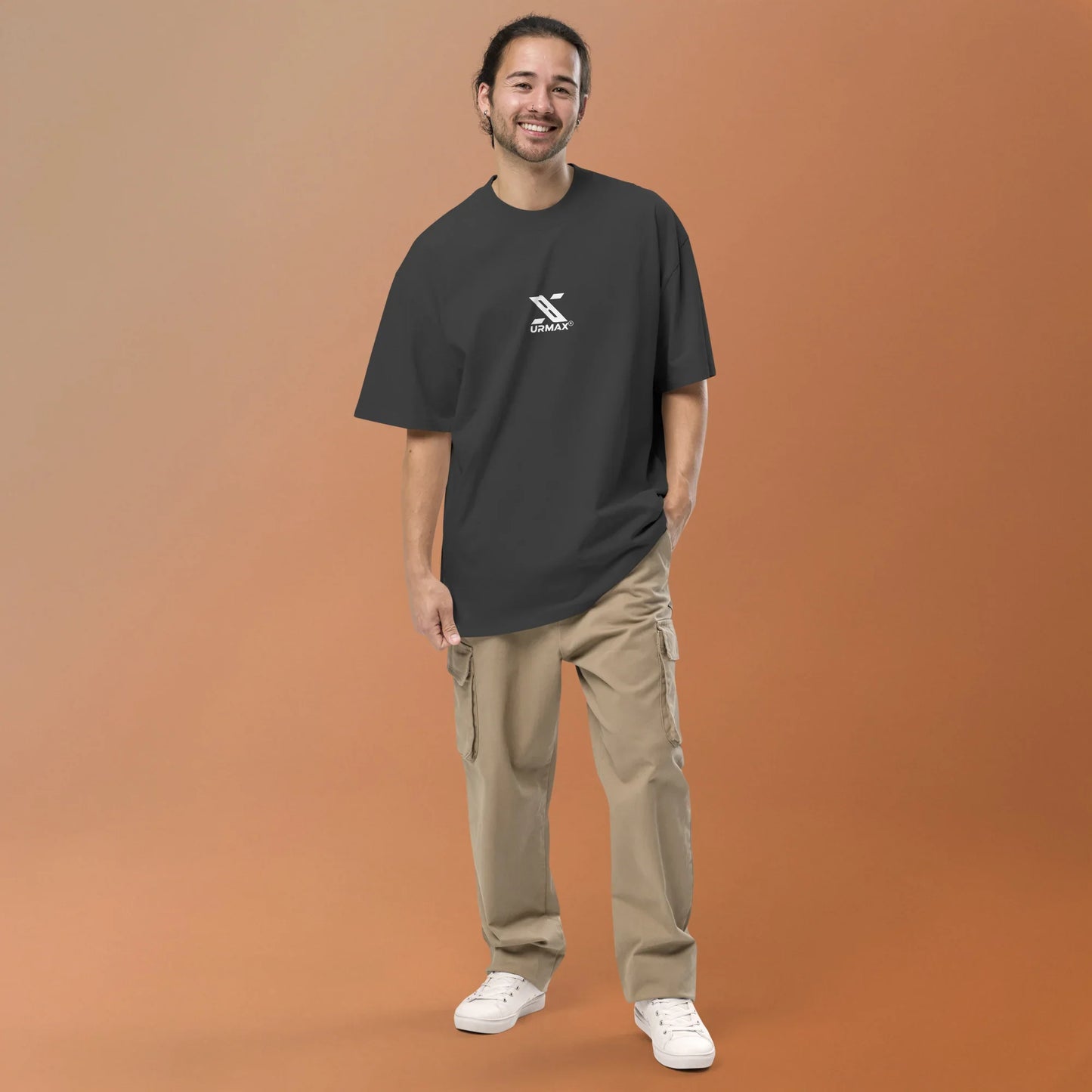 Man in oversized faded black Urmax t-shirt and cargo pants standing on brown background