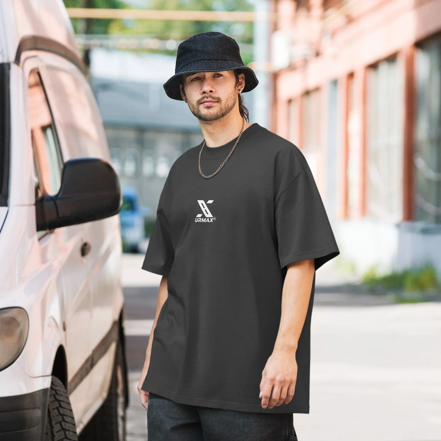 Man in oversized faded black URMAX t-shirt and bucket hat standing outdoors near a van